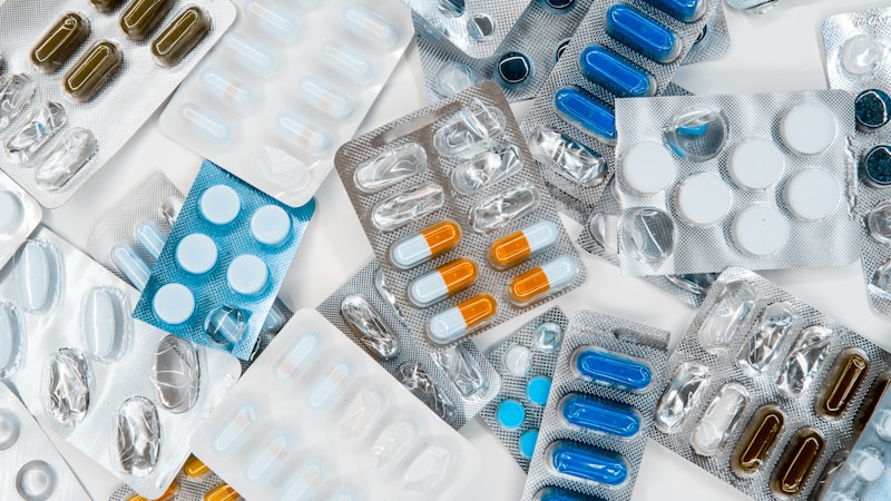 Pharmacist reviewing medication labels behind a pharmacy counter with shelves of prescription bottles